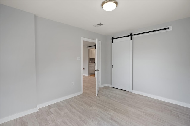 unfurnished bedroom featuring a barn door and light hardwood / wood-style floors