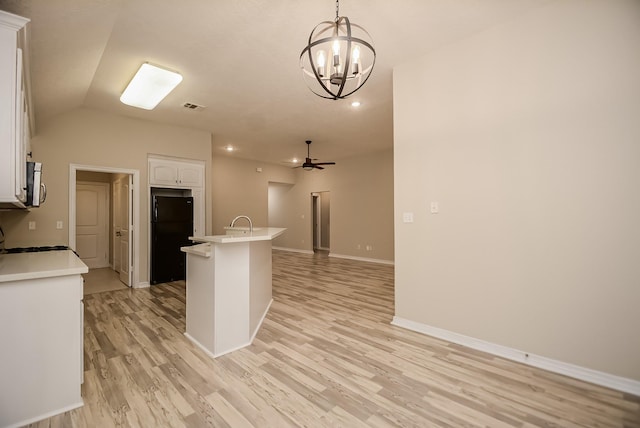 kitchen with lofted ceiling, ceiling fan with notable chandelier, black fridge, decorative light fixtures, and white cabinetry