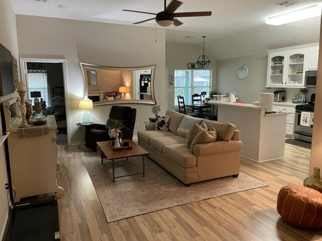 living room featuring light wood-type flooring, vaulted ceiling, ceiling fan, and sink