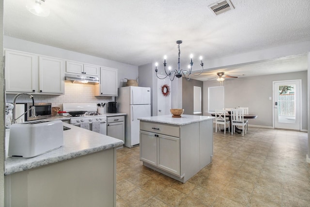 kitchen with tasteful backsplash, ceiling fan with notable chandelier, white appliances, decorative light fixtures, and a kitchen island