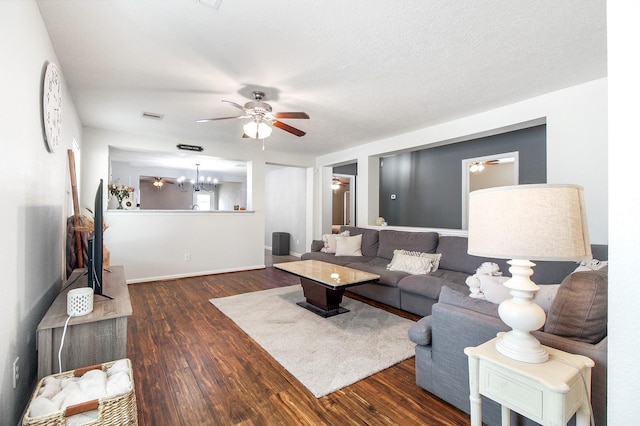 living room with a textured ceiling, ceiling fan with notable chandelier, and dark wood-type flooring