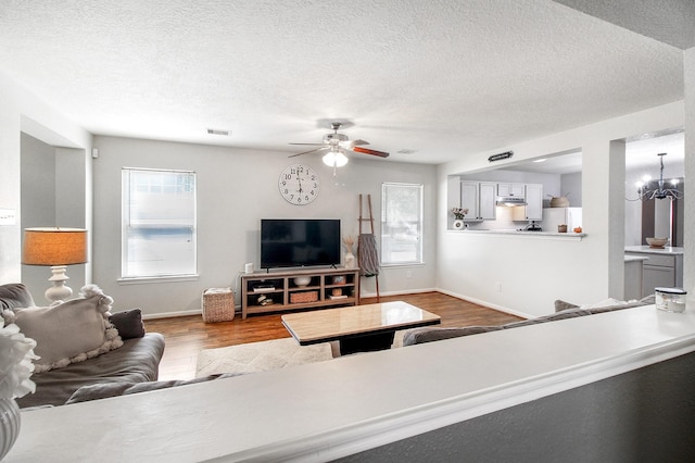 living room featuring ceiling fan with notable chandelier, a textured ceiling, and hardwood / wood-style flooring