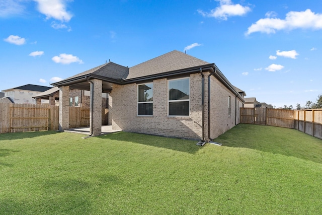 back of house featuring a fenced backyard, a lawn, brick siding, and roof with shingles