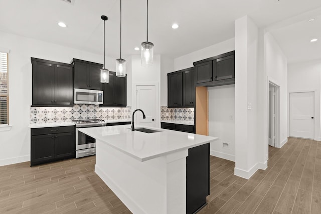 kitchen with a center island with sink, appliances with stainless steel finishes, dark cabinets, light countertops, and a sink