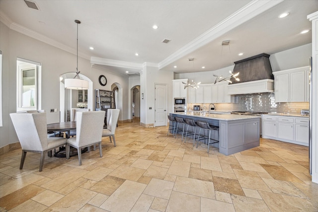 kitchen with a breakfast bar, pendant lighting, white cabinets, custom range hood, and a center island with sink