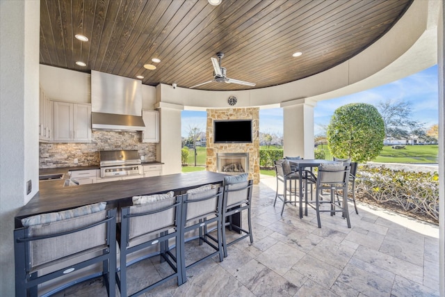 view of patio featuring a bar, a grill, area for grilling, an outdoor stone fireplace, and ceiling fan