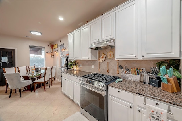 kitchen with decorative backsplash, dark stone countertops, white cabinets, stainless steel gas stove, and light tile patterned flooring