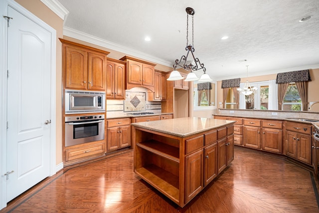 kitchen with crown molding, appliances with stainless steel finishes, decorative light fixtures, and a kitchen island