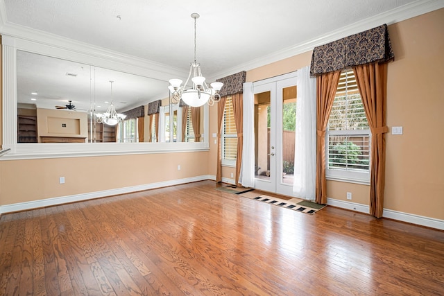 unfurnished dining area featuring wood-type flooring, crown molding, an inviting chandelier, and french doors