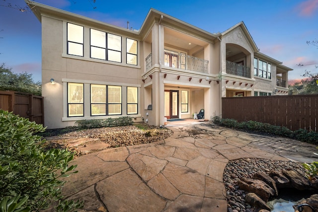 back house at dusk with a patio and a balcony