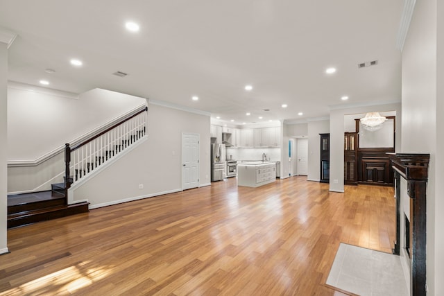 unfurnished living room with light hardwood / wood-style floors, an inviting chandelier, ornamental molding, and sink