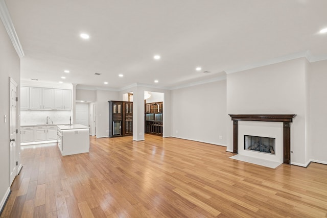 unfurnished living room featuring light wood-type flooring, ornamental molding, and sink