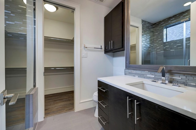 bathroom featuring walk in shower, tasteful backsplash, tile patterned flooring, toilet, and vanity