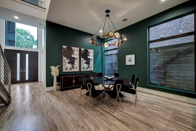 dining area featuring a chandelier, light hardwood / wood-style floors, a high ceiling, and french doors