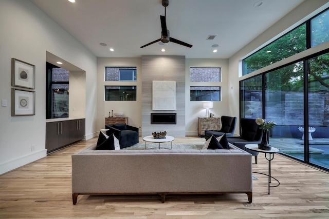 living room featuring a large fireplace, light hardwood / wood-style flooring, and ceiling fan