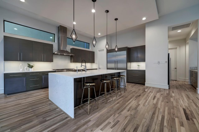 kitchen featuring pendant lighting, a kitchen island with sink, sink, light hardwood / wood-style flooring, and wall chimney exhaust hood