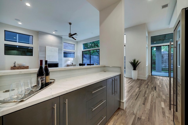 kitchen with ceiling fan, light stone counters, and light hardwood / wood-style flooring