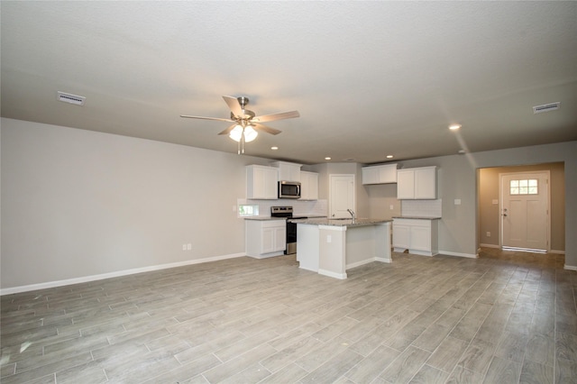 kitchen featuring a kitchen island with sink, white cabinets, stainless steel appliances, and light stone counters