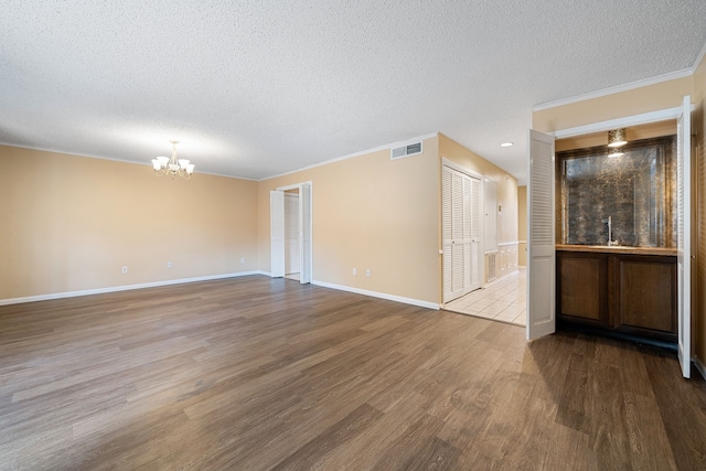 empty room featuring wood-type flooring, a textured ceiling, an inviting chandelier, and crown molding