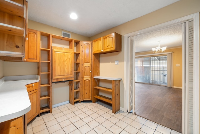 kitchen with ornamental molding, a textured ceiling, pendant lighting, a notable chandelier, and light tile patterned flooring