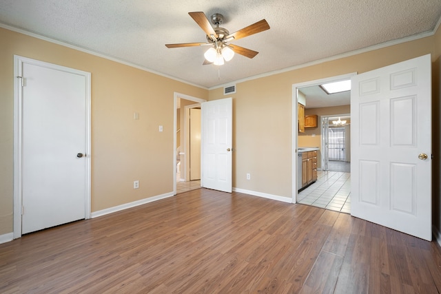 unfurnished bedroom with light wood-type flooring, ensuite bathroom, a textured ceiling, ceiling fan, and crown molding