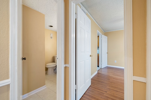 hall with light hardwood / wood-style floors, a textured ceiling, and ornamental molding