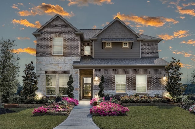 view of front of home with brick siding, stone siding, a shingled roof, and a front yard