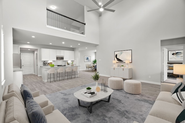 living room featuring light wood finished floors, baseboards, a high ceiling, and ceiling fan