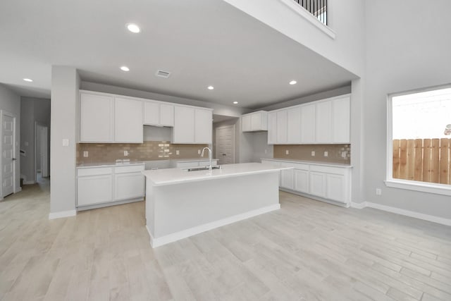kitchen featuring a sink, a kitchen island with sink, backsplash, white cabinetry, and visible vents