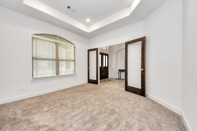 unfurnished bedroom with french doors, light carpet, and a tray ceiling