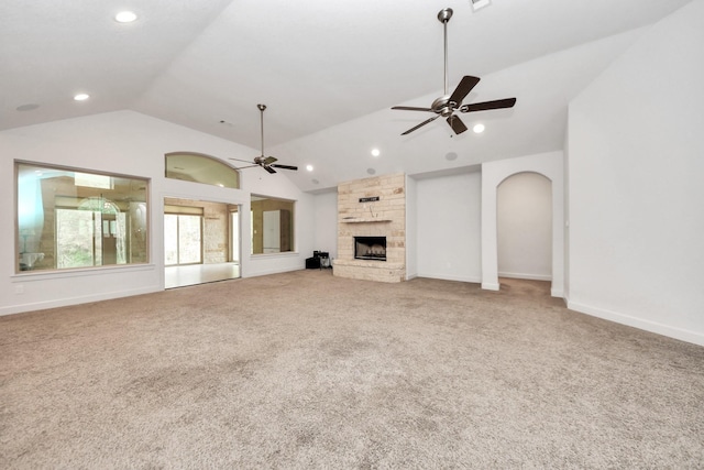 unfurnished living room with ceiling fan, a stone fireplace, lofted ceiling, and carpet floors