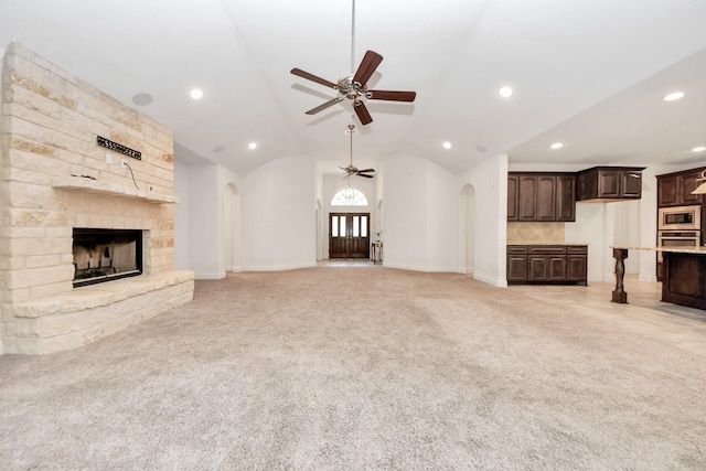 unfurnished living room with ceiling fan, light colored carpet, vaulted ceiling, and a fireplace