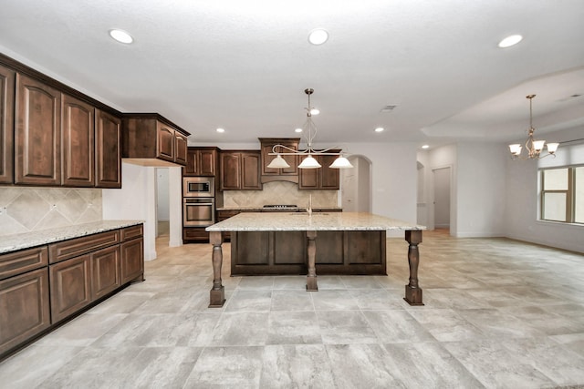 kitchen featuring decorative backsplash, dark brown cabinets, a center island with sink, pendant lighting, and appliances with stainless steel finishes