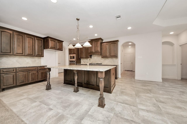 kitchen with stainless steel appliances, dark brown cabinetry, a center island with sink, and hanging light fixtures