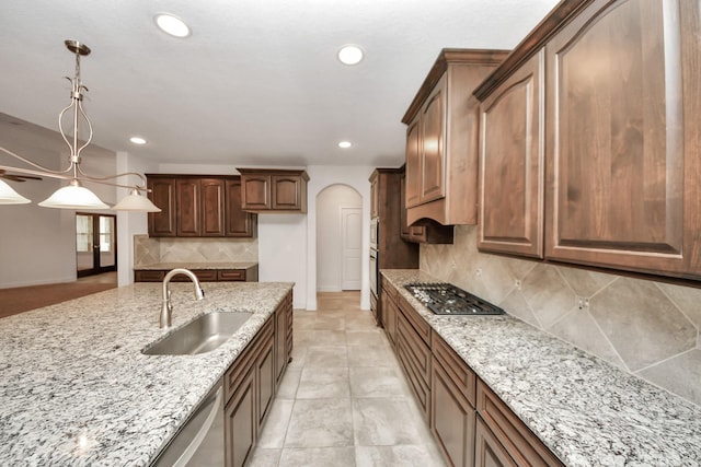 kitchen with stainless steel appliances, light stone countertops, sink, decorative light fixtures, and tasteful backsplash