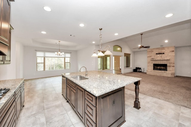 kitchen featuring decorative light fixtures, a center island with sink, light colored carpet, a fireplace, and sink