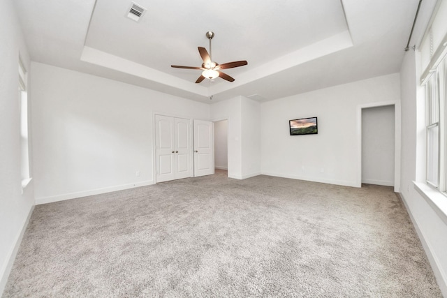 unfurnished bedroom with ceiling fan, a tray ceiling, a closet, and carpet