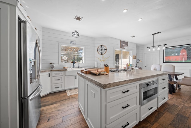 kitchen with appliances with stainless steel finishes, dark hardwood / wood-style flooring, sink, white cabinets, and a center island