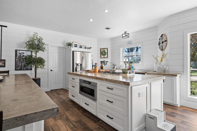 kitchen featuring white cabinetry, built in microwave, a center island, a healthy amount of sunlight, and dark wood-type flooring