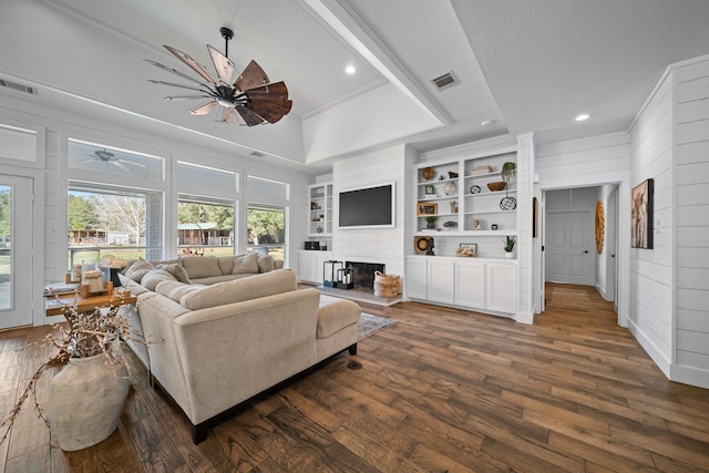 living room featuring a raised ceiling, wooden walls, ceiling fan, built in shelves, and dark hardwood / wood-style floors