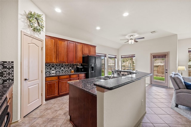 kitchen with a kitchen island with sink, backsplash, light tile patterned floors, and black fridge