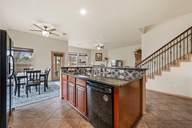 kitchen featuring dark stone countertops, sink, black appliances, and a center island with sink