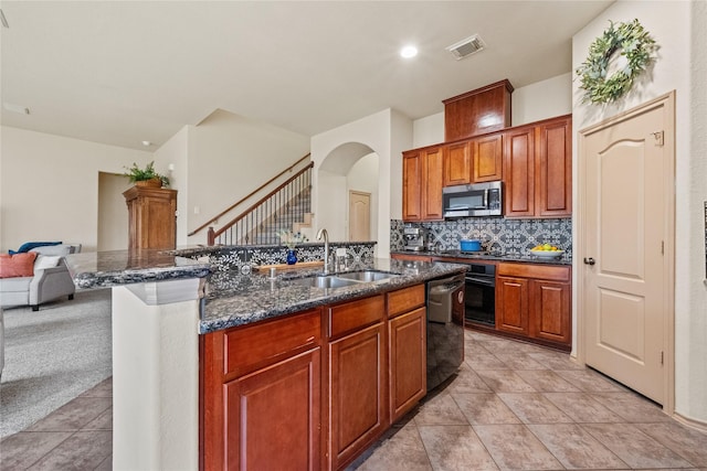 kitchen featuring sink, black appliances, an island with sink, decorative backsplash, and dark stone counters