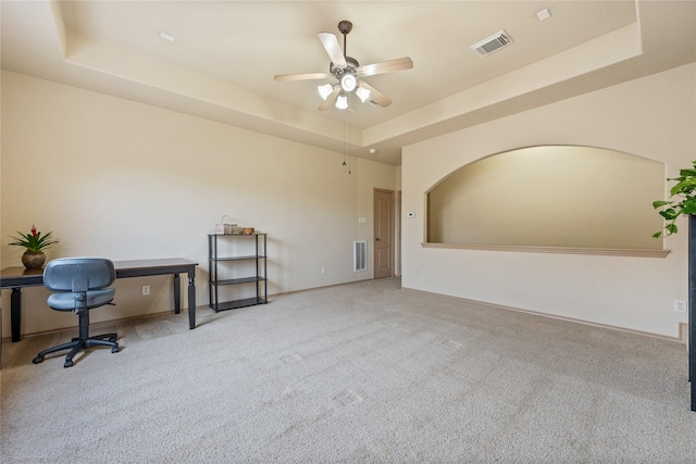 office area featuring light colored carpet, a raised ceiling, and ceiling fan