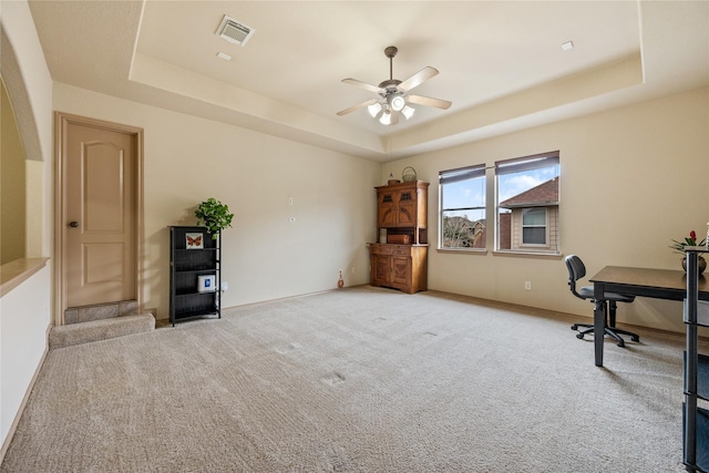 unfurnished office featuring ceiling fan, a raised ceiling, and light carpet