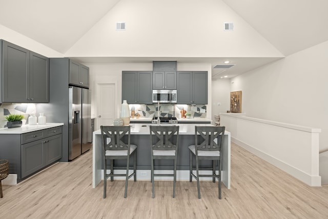 kitchen featuring a breakfast bar, backsplash, appliances with stainless steel finishes, and gray cabinetry