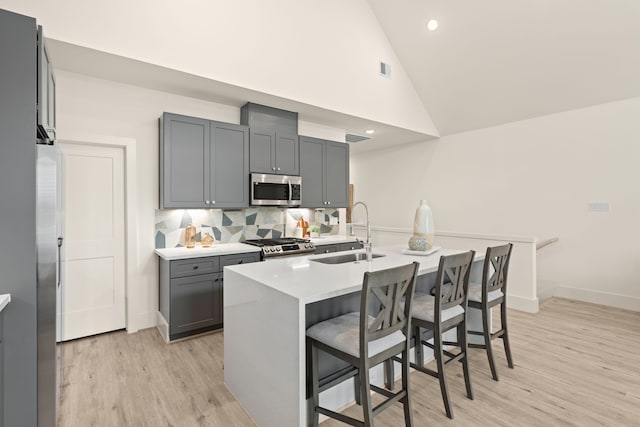 kitchen with an island with sink, a breakfast bar area, appliances with stainless steel finishes, gray cabinetry, and sink