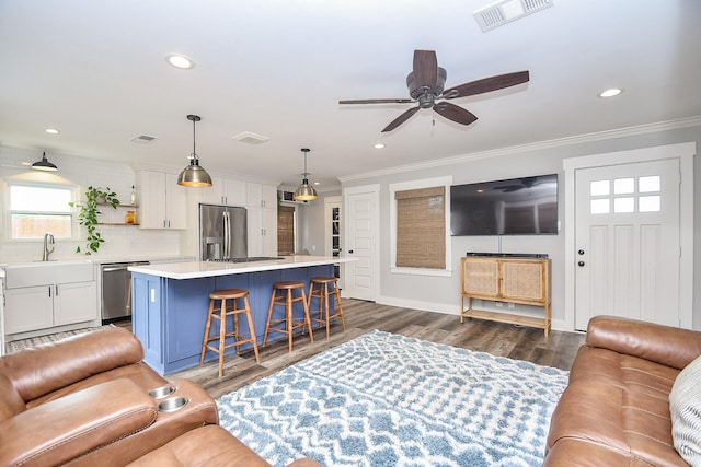 living room with ceiling fan, sink, dark wood-type flooring, and ornamental molding