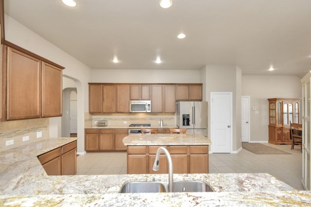 kitchen featuring a kitchen island with sink, sink, light tile patterned floors, appliances with stainless steel finishes, and light stone counters