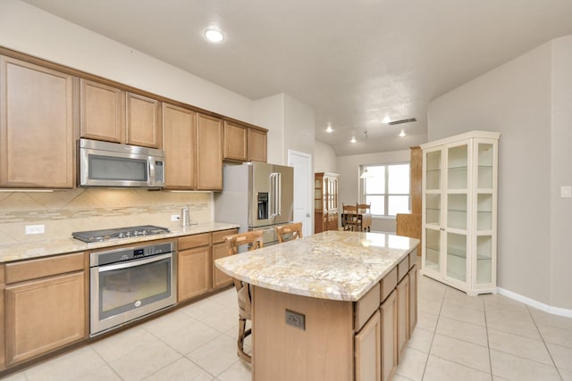 kitchen with a center island, stainless steel appliances, a kitchen breakfast bar, tasteful backsplash, and light stone counters